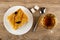 Cake with jam and prune in plate, sugar cubes, spoon, cup with tea on wooden table. Top view