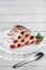 Cake from rolled pancakes with cream, cherries and grated chocolate on plate, on a light wooden background