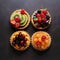 Cakes on a dark marble table, top view. Four tartlets with different fruits and berries. Generative AI