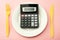 Calculate expensive food spending costs, counting calories and weight loss program concept with calculator onn empty plate, yellow