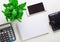 Calculator, blank notebook, phone, wallet and green plant on a light table. Workplace close-up. Flat lay. Copy space