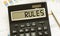 A calculator labeled RULES lies on financial documents in the office