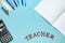 Calculator, notebook, writing supplies and word teacher on blue surface