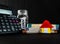 Calculator with a zero, coin filled glass jar, note bundles and a toy house against black background