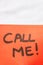 Call me handwriting text close up isolated on orange paper with copy space. Writing text on memo post reminder