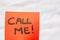 Call me handwriting text close up isolated on orange paper with copy space. Writing text on memo post reminder