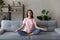 Calm Arabian woman meditating, sitting in lotus pose on couch