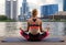 Calm athletic girl meditating at sunset against background of a pond and passing kayaker. Against evening sky.