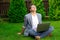 Calm and balanced businessman sits cross-legged on grass with laptop closed eyes