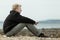 Calm blond teen sitting on rocky beach