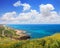 Calm blue sea landscape. Stony seashore. Bright yellow flowers grow on rocky cliff. Sunny seascape with impressive blue sky