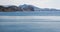 Calm blue sea with little ripples on the surface, mountains and houses on the horizon.