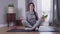 Calm brunette Caucasian woman sitting with eyes closed on yoga mat. Young woman calming down after hard day. Lifestyle