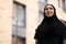 Calm confident young pretty middle eastern woman in hijab look at empty space on city building background