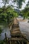 Calm and in depth view of natural landscape during the daylight, with focus on a broken wooden bridge crossing a clear