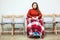 Calm disabled woman in wheel-chair with blanket on legs looking at camera while sitting in room