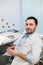 Calm doctor or consultant sitting at desk with his stethoscope on table looking to the camera