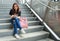 Calm ethnic Asian female sitting with backpack on staircase underground and browsing mobile phone. City life travel and