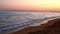 A calm evening sea waves in a bay with a sandy beach on a sunset background.