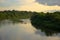 The calm flow of the forest river along the banks overgrown with tall trees with reflecting clouds. Landscape