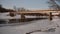 Calm frozen river stream underneath metal car bridge in winter with white snow on the shore sides