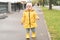 Calm funny toddler baby girl 2 years old in yellow raincoat walking on the asphalt road in raining day. Stylish girl is wearing