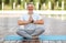 Calm happy mature man sitting in lotus pose on mat during morning meditation in park