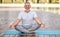 Calm happy senior man sitting in lotus pose on mat during morning meditation in park