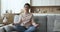 Calm Indian woman do meditation seated on sofa at home