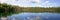 Calm lake surrounded by trees panorama