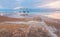 Calm morning at Ein Bokek Dead Sea beach, pink clouds reflection over water surface near steel rails leading to sun shade shelter