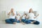 Calm mother with closed eyes meditating in lotus pose on floor, stressed father and two tired children in living room at home