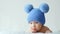 A calm newborn baby in a blue hat with pompoms looks into the camera. A sweet two-month-old infant is lying on a blanket. A
