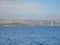 Calm ocean with glistening water and a coastal town and mountains with windmills in the horizon