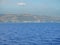 Calm ocean with glistening water and a coastal town and mountains with windmills in the horizon