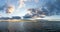 Calm ocean waters under an expressive sky at sunset with mountain silhouette in the background