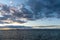 Calm ocean waters under an expressive sky at sunset with mountain silhouette in the background