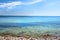 Calm ocean waves washing onto stones at an empty beach shore with sailboats cruising in the horizon. Scenic landscape