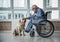 Calm old male on wheelchair stroking the pooch in room