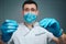 Calm peaceful young make dentist in uniform and mask. He look on camera and hold dental tools. Guy wear latex gloves