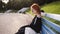 Calm red headed girl using a smart phone in a city park sitting on a bench, young woman in black dress and white bag