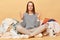 Calm relaxed Caucasian woman posing near heap of multicolored unsorted clothes isolated over beige background meditating