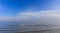 Calm sea and blue sky with white clouds background. An airplane fly on the horizon.