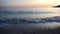 Calm sea surf in the foreground and a small boat with two fishermen against the pink sunset sky.