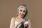 Calm smiling old european lady with gray hair in towel holding jar of moisturizer cream