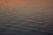 Calm smooth water on sunset with orange, pink, yellow reflection and glare of sun on blue water, texture, background.