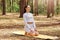 Calm sporty female enjoying fresh air while training in forest, keeping eyes closed, sitting on gym mat practicing yoga,