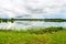 Calm water of lake, woods on other side and blue sky.