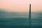 Calm water with solitary wooden post and reflection. Serene image.