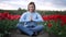 Calm woman relaxing, meditating in tulips field alone. Girl calms down, breathes deeply with mudra om, namaste. Inner